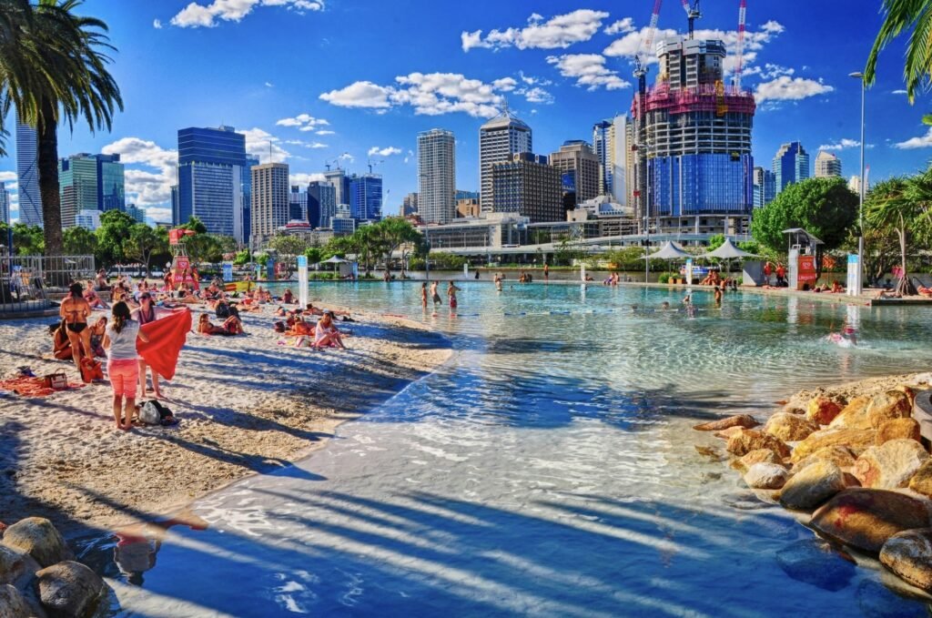 People relaxing on a sandy beach in Brisbane during daytime, with clear blue water and bright sunshine.