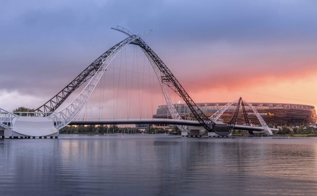 Matagarup Bridge in Perth, Western Australia, spanning across the Swan River at sunrise with soft purple and brown tones.