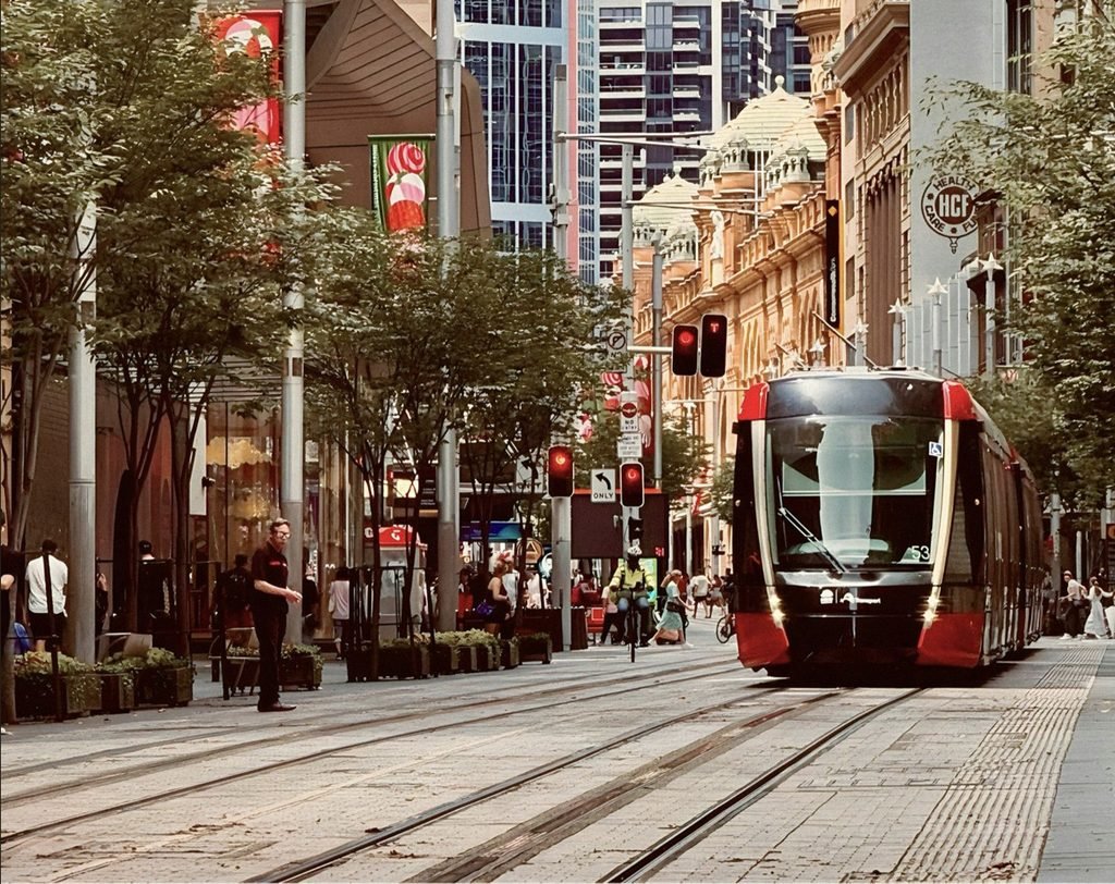 A red and white Sydney tram travelling along George Street with tall city buildings in the background.