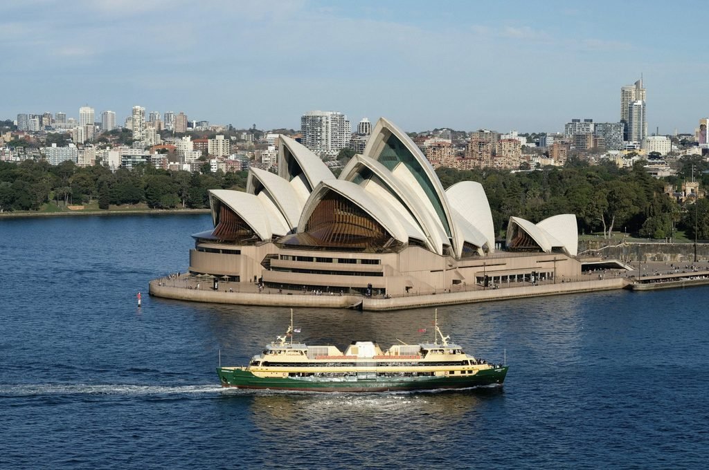 A peaceful harbour moment in Sydney, featuring a lone boat drifting near the iconic Opera House with the Harbour Bridge towering behind.