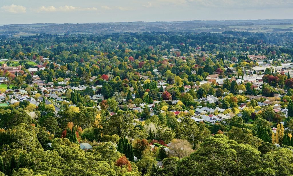 An aerial view of Bowral, surrounded by autumn‑coloured trees under a cloudy sky -  part of the Southern Highlands region.