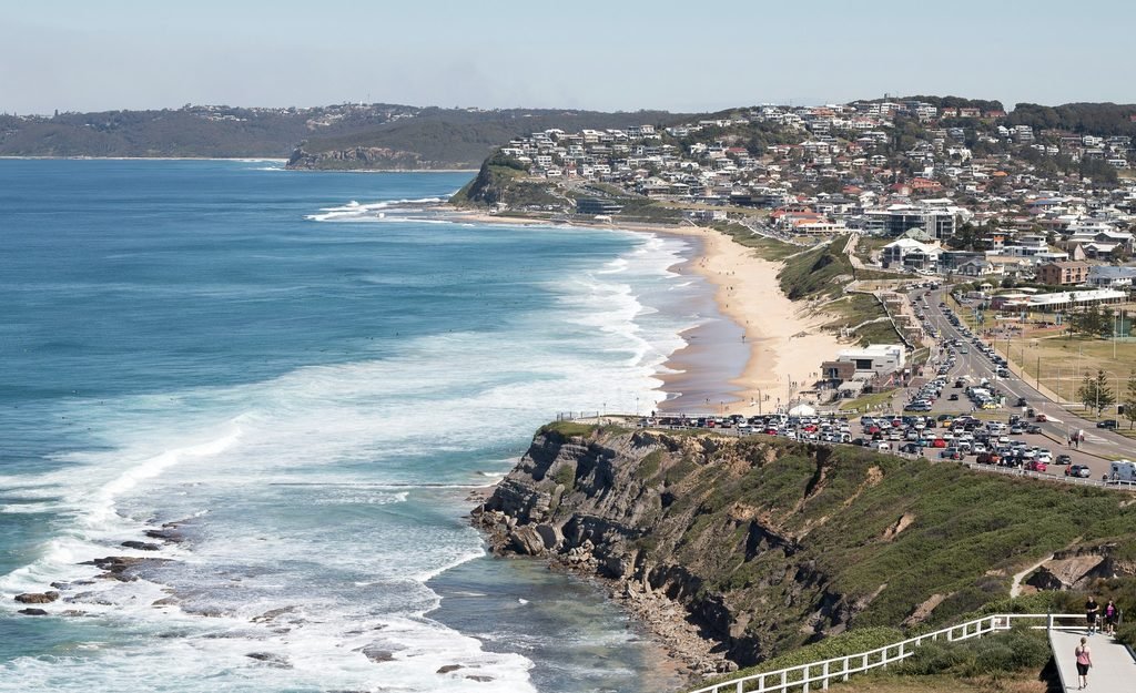 This aerial photo shows Newcastle NSW, where the city meets the Pacific Ocean. You can see the coastline curving around sandy beaches, rocky headlands and a bright blue waterfront, with the urban grid stretching inland. It captures Newcastle’s classic mix of surf beaches, harbour views and relaxed coastal city energy.