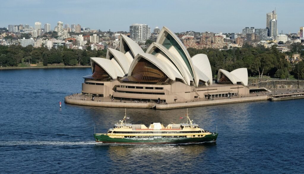 A Sydney Harbour ferry glides across calm blue water with the Harbour Bridge and Opera House in the background, showcasing easy public transport access around the harbour.