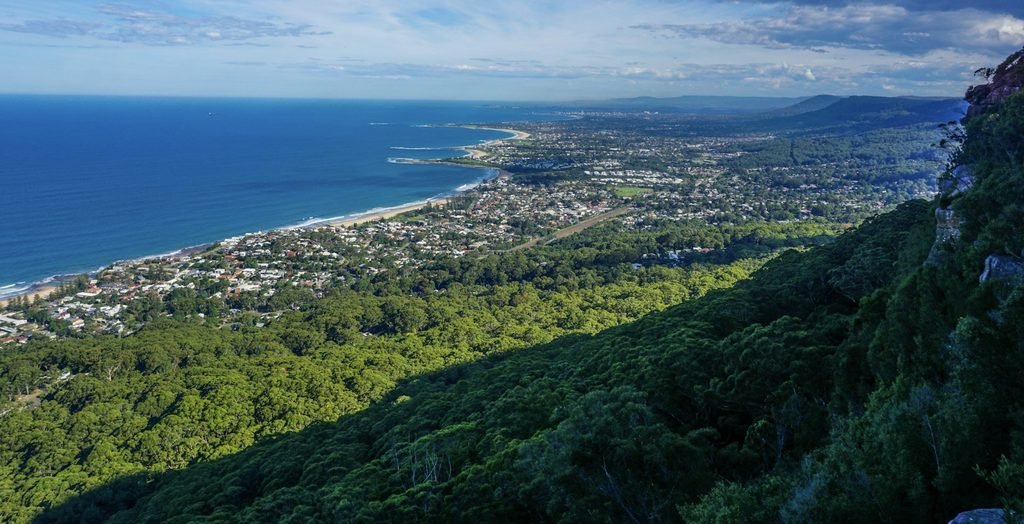 A panoramic view from Sublime Point Lookout overlooking the Illawarra escarpment, with green bushland, the Pacific Ocean and Austimer Beach curving along the coastline below.